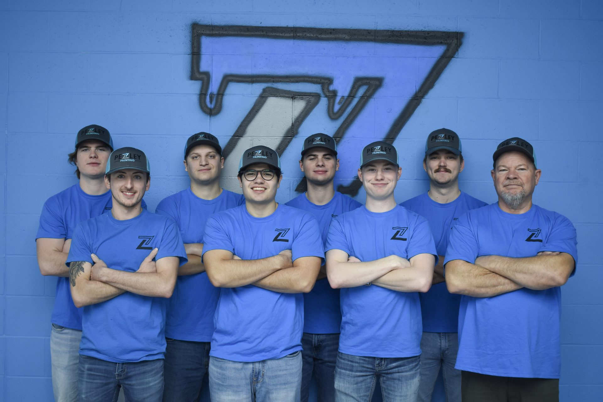 The Pezley Painting crew in branded blue shirts in front of the company logo wall